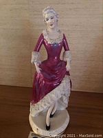 Front view of Staffordshire 'Christina' figurine showing seated woman in maroon dress with lace detail and black shoes.