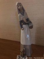 Full view of the Lladro figurine showcasing the girl with bread basket and puppy on a wooden surface.