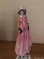 Front view of the Royal Doulton figurine depicting a woman in a long pink dress with a feathered hat and black gloves.