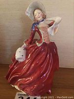 Front view of the Royal Doulton 'Autumn Breezes' figurine showing the detailed flowing red dress, hat and muff.