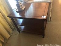 Image showing one of the two walnut finish side tables placed next to a window with a lamp on top, highlighting its surface and lower shelves.