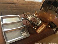 A wide shot showing all items in the lot including the stainless steel trays, condiment set, glass bowl, assorted decorative items on wood table