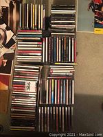 Top view of multiple stacks and rows of music CDs laid out on carpet.