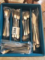 Blue plastic tray holding wrapped and loose stainless steel flatware: knives, forks, spoons and teaspoons