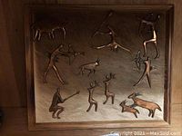 Full view of copper figures artwork mounted on wood showing multiple Bushmen figures and animals in various poses.