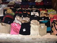 Overview of ladies tops laid out on a bed showing multiple rows in various colors and styles including solids and stripes.