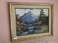 Framed landscape painting showing mountain, waterfall and forest in gold ornate frame