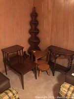 Wide view showing corner curio shelf against wall, three tables with different leg styles, small stool and magazine basket arranged in corner on carpeted floor.