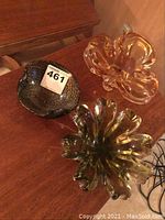 Three mid century modern art glass dishes on wood table: amber ruffled dish, green ruffled dish, and black speckled Chalet dish.