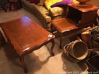 Leather top coffee table and stepped leather top side table shown side by side on carpeted floor near sofa and baskets.