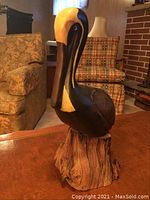 Front-left angled view of the carved wooden pelican on table with living room background showing detail on body and face.