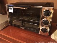 Front view of Delonghi convection toaster oven showing glass door, metal handle, and control knobs.