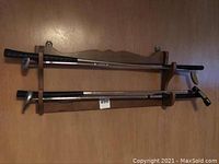 Wide view of four golf putters on a wooden wall-mounted rack, showing all putters horizontally aligned with black grips and metal shafts.