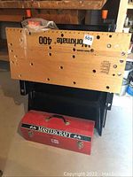Portable wooden workbench with holes and Black & Decker Workmate 400 branding, standing upright with a red toolbox beneath it