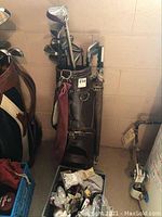 Brown golf bag filled with golf clubs standing against wall, with blue crate containing accessories in front