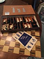 Opened box showing organized chess pieces in black and white, chessboard beneath, and instruction booklet.
