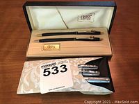 Two black Cross pens with gold trim in their original box with 'Cross' branding, along with a black sheath containing three Sheaffer pens with white dot on clip.