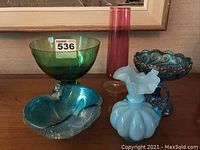 Five decorative glass pieces on wooden surface with various shapes and colors including green, red, blue, and amber.