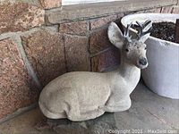 Cement deer statue sitting on ground next to planter