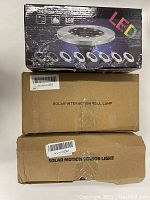 Boxes of solar ground LED lights, solar interaction wall lamps, and solar motion sensor lights stacked for lot overview.