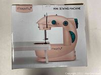 Front of Magicfly Mini Sewing Machine box showing image of the compact pink machine with teal details.