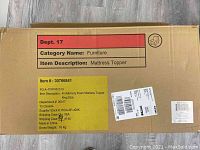 Closed cardboard box showing item description label for mattress topper.