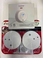 Front view of XSENSE SC01 smoke and carbon monoxide alarm sealed boxed and two Kiddie i9060CAKT smoke alarms in original packaging, two open boxes