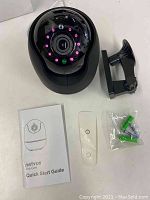 Netvue Orb camera with surrounding IR LEDs, black adjustable wall mount, clear mounting plate, wall anchors and screws, and Quick Start Guide manual arranged on a flat surface.