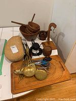 Photo showing wooden bowls, cutting board with brass spoons and olive forks, scissors, and a candle warmer.