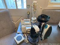Full lot collection showing Braun immersion blender, two Sunbeam mixers, mug warmer, Ninja blender, and SilverStone iron all on table.
