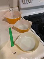 Three Pyrex yellow and white mixing bowls in different sizes lined up on a counter near stove, showing front view and side pouring spouts.