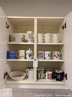 Cabinet shelf showing assortment of 12 mugs with varied designs and a bowl on the lower shelf with floral pattern