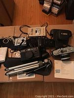 Overview of all cameras, tripod, case, straps, cables and manuals on tabletop