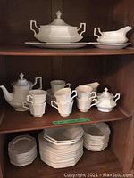 Image showing middle and lower shelves with teapot, cups, sugar bowl, creamer, and stacks of plates and saucers.