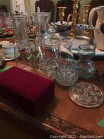 Photo showing assortment of glass vases and jars on a table, and a set of silver spoons in a red box.