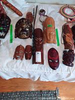 Top-down photo showing a variety of carved wooden masks and decor items arranged on a white cloth.