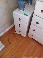 Photo of white 3-drawer side table with two blue lamps on top, showing brass keyhole escutcheons and some scratches.