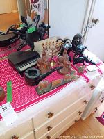 Photo showing various carved wooden bookends, animal figurines, a brass menorah, a large carved pipe, and black carved figures on a red and white cloth-covered dresser.