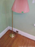 Full view of one floor lamp showing brass base, pole, and pink pleated lampshade