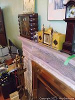 Overall view of a mantle with Long Branch Saloon style clock, yellow vintage clocks, and packing materials