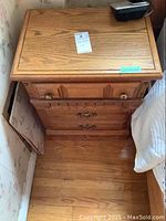 First photo showing one oak night table with two drawers against a wall and bedside, with visible wear on wood surface.