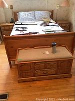 Full view of pine bed with floral bed linens, with wooden nightstands on each side and wooden storage bench at foot of bed.
