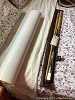 Photo showing the brown leather case containing folded pool cue and rolled Saudi Arabia posters on a floral patterned bed spread