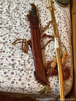 Top view of machete in brown leather sheath and ceremonial sword with gold-colored metal sheath placed side by side on patterned fabric.