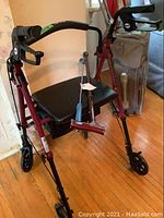 Red drive walker with padded seat, showing attached wooden cane and blue-handled shoe horn.