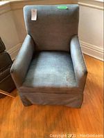 Front view of a medium grey velour upholstered arm chair with padded arms and skirted bottom. Fabric shows wear and minor discoloration.