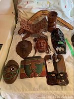 Top view of all items laid out on a white surface, showing five wood carved masks, a painted wooden boomerang, an ornately carved headrest, and a turned wooden candle holder.