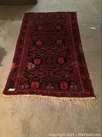 Full view of rectangular Persian wool rug with deep red and black geometric pattern lying flat on carpeted floor.