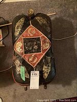 Top view of a black embossed leather folding stool with red and gold decorative accents and a wooden base, showing wear.