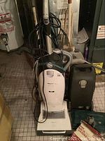 Photo of white Miele Mistral vacuum showing power dial and cord wrapped on handle with other floor cleaners nearby